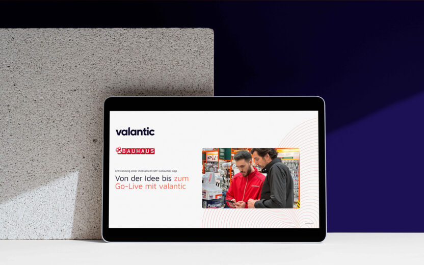 Mockup der Referenz BAUHAUS: Ein Tablet zeigt eine Präsentationsfolie mit den Logos von valantic und BAUHAUS und einem Foto von zwei Personen beim Einkaufen, begleitet von einem deutschen Text über App-Entwicklung und Kundenerfahrung in der Logistik.