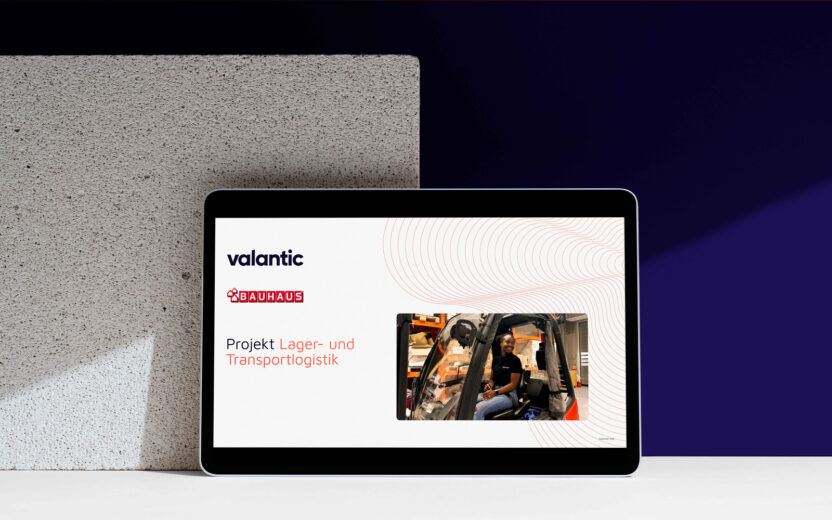 Mockup valantic Referenz BAUHAUS, Projekt Logistik: Auf einem Tablet ist eine Präsentationsfolie mit den Logos von Valantic und Bauhaus zu sehen, die den Titel "Projekt Lager- und Transportlogistik" trägt und Logistiklösungen sowie das Foto einer Person zeigt, die eine Lagereinrichtung bedient.