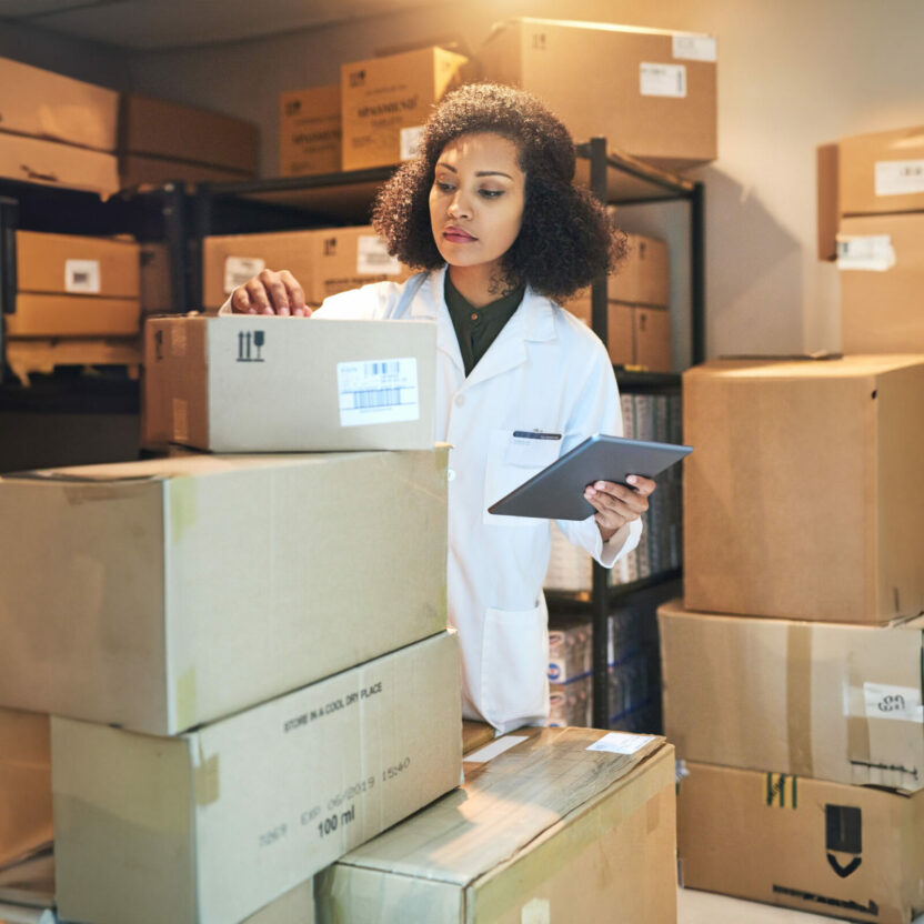 A woman standing in the warehouse, wearing a white coat and checking cardboard boxes