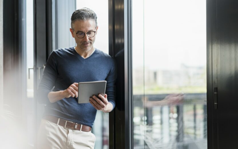 A man with glasses stands by a window, using a tablet device to review it security protocols.