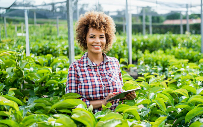 A woman stands in a green greenhouse and checks data on her Ipad