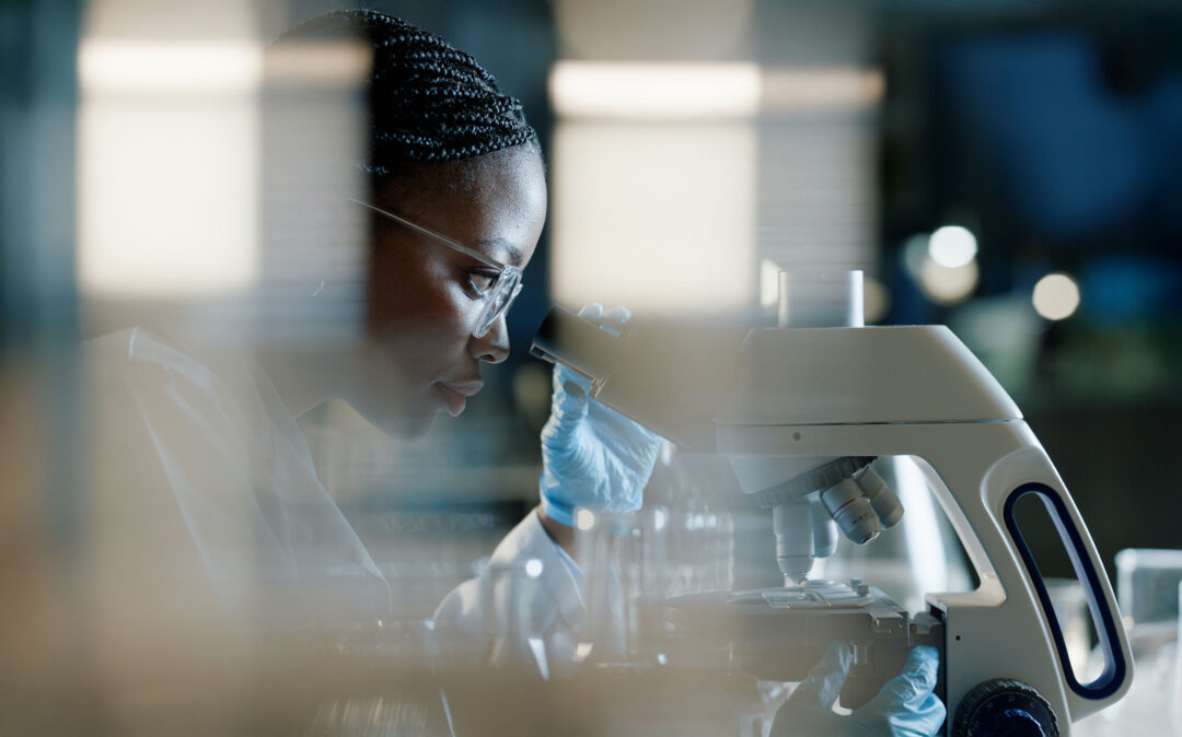 Ein Wissenschaftler mit Handschuhen und Schutzbrille schaut in einem Labor in ein Mikroskop.