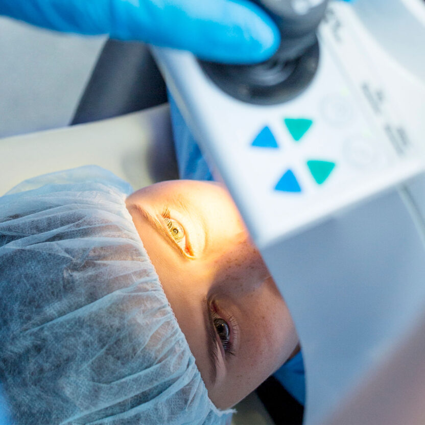 Ein Patient liegt während einer Augenuntersuchung oder eines Eingriffs unter einem medizinischen Gerät, wobei ein helles Licht auf sein offenes Auge gerichtet ist.