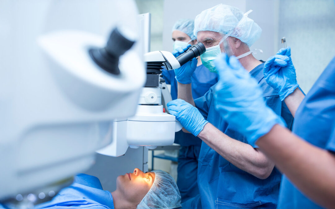 Ein Chirurg benutzt ein Mikroskop, während er eine Augenoperation an einem liegenden Patienten durchführt, während das medizinische Personal in einem Operationssaal assistiert.