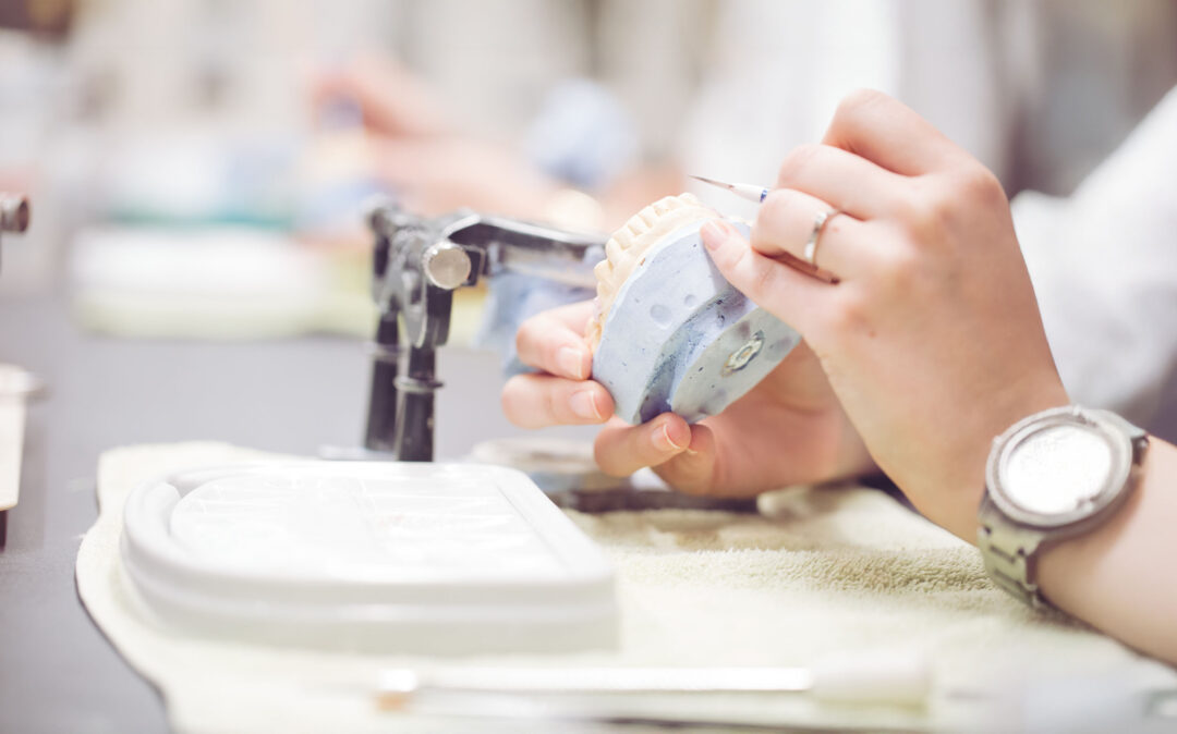 Eine Person arbeitet mit einem Werkzeug an einer Zahnform, hält die Form in einer Hand und trägt eine Armbanduhr.