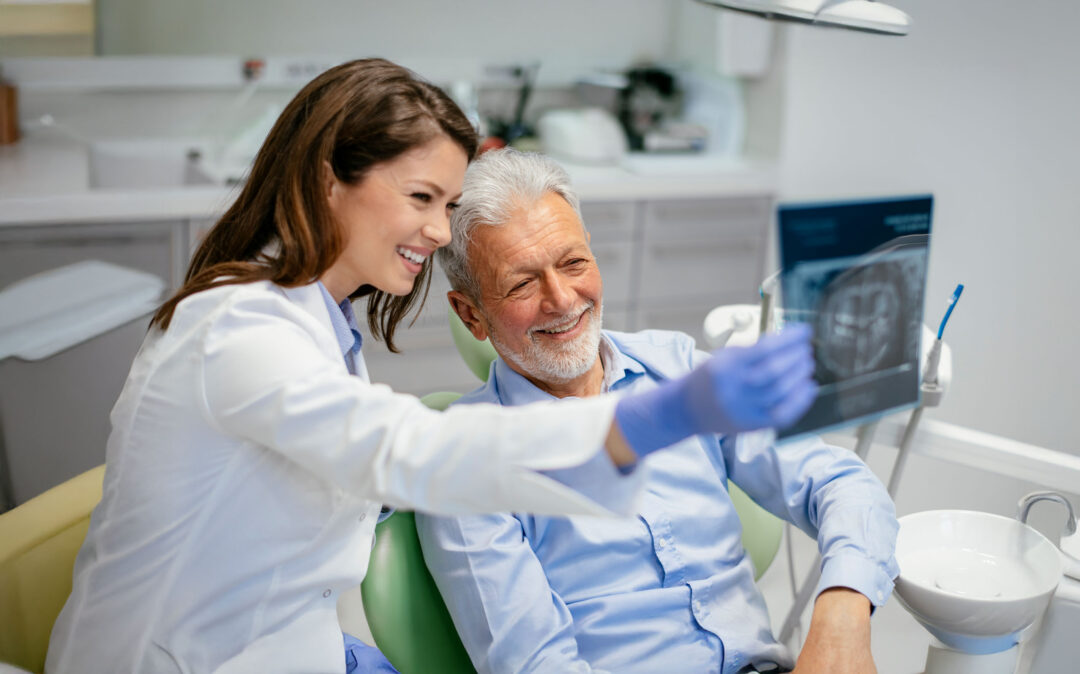 Ein Zahnarzt und ein älterer männlicher Patient sehen sich gemeinsam ein Röntgenbild in einer Zahnarztpraxis an.