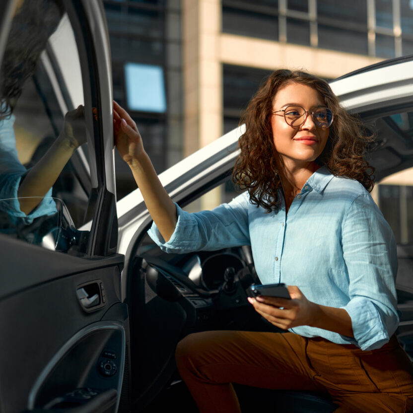 Business woman sitting in her new car and using smartphone.