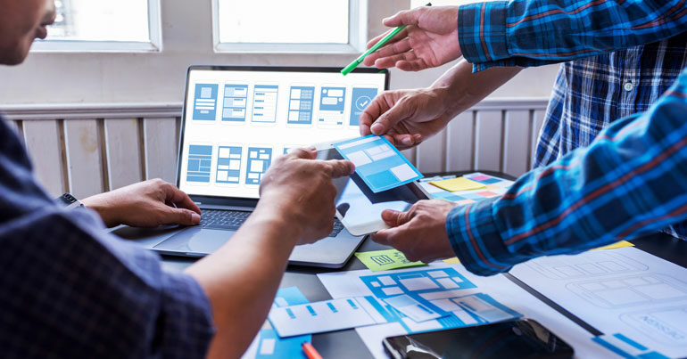 Zwei Personen arbeiten gemeinsam an einem Laptop und betrachten Baupläne im Rahmen eines UX-Teams.