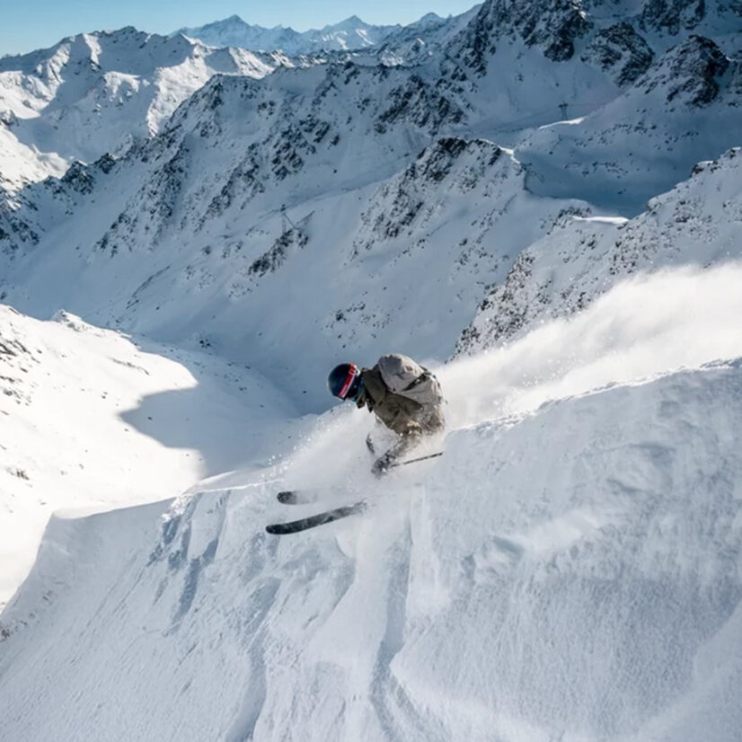 Freerider in Verbier fährt eine steile Pulverschnee-Abfahrt hinunter, umgeben von einer spektakulären Alpenlandschaft.