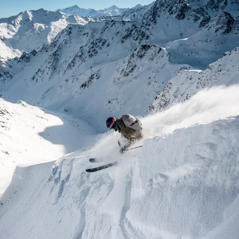 A freerider in Verbier rides down a steep powder slope, surrounded by spectacular Alpine scenery.