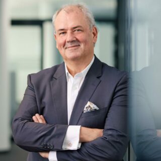 Bernd Wagner, CEO of STACKIT Cloud, standing confidently with arms crossed in a dark suit and white shirt, smiling slightly in a modern office environment.