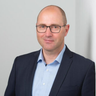 Nico Michels, Head of Digital Enterprise & Academics at Siemens Digital Industries Software, wearing glasses, a light blue shirt, and a dark suit jacket.