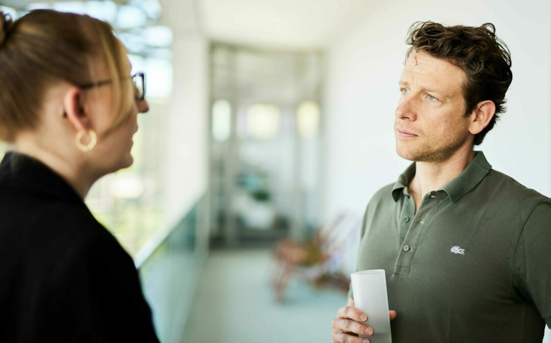 Ein Mann und eine Frau führen ein Gespräch über Magento-Projekte in einem Bürogebäude.