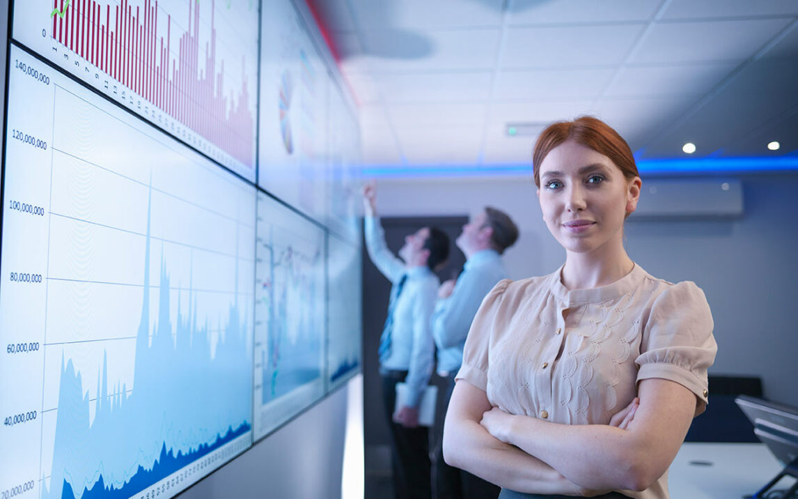 Woman in the office, projection on whiteboard, two men discussing in front of it, cool blue tones.