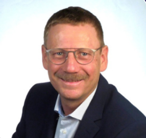 Jens Stapelfeldt, Global AI Lead at AMD, smiling in a professional portrait wearing glasses, a white shirt, and a dark jacket.
