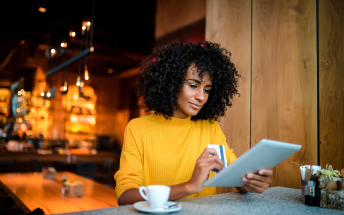 Beautiful smiling African American woman using digital tablet at the bar.