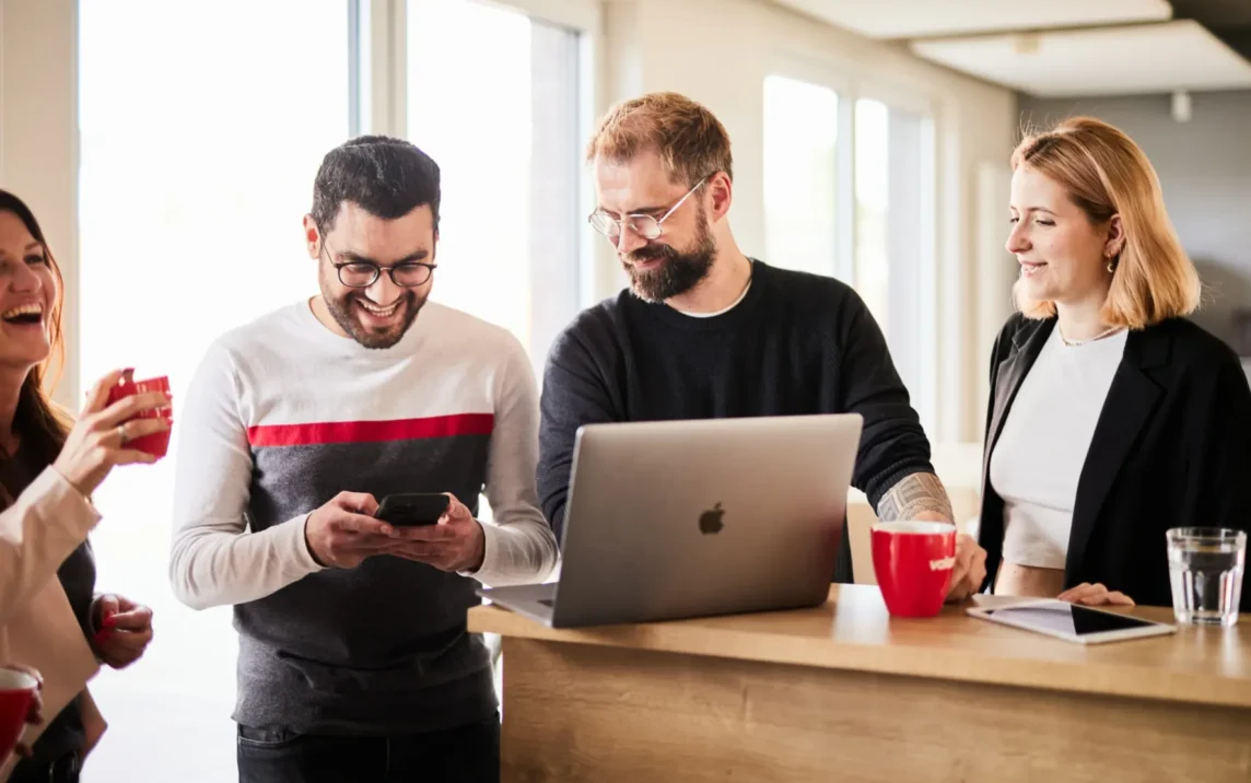 Ein Team von Personen, die in einem Büro an einem Laptop arbeiten und mit Hilfe von KI-Technologie eine Diskussion führen.