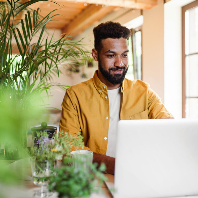 Young man with laptop and coffee working indoors, home office concept.