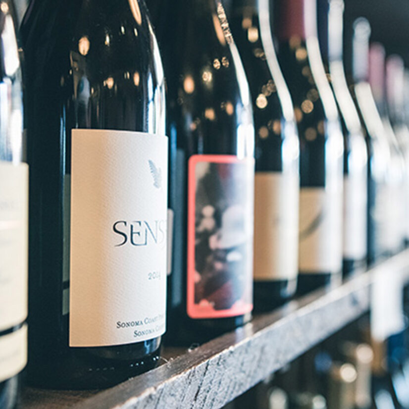 Nahaufnahme mehrerer Weinflaschen in einem Regal, Fokus auf das Etikett einer Flasche mit der Aufschrift „Sensi“.