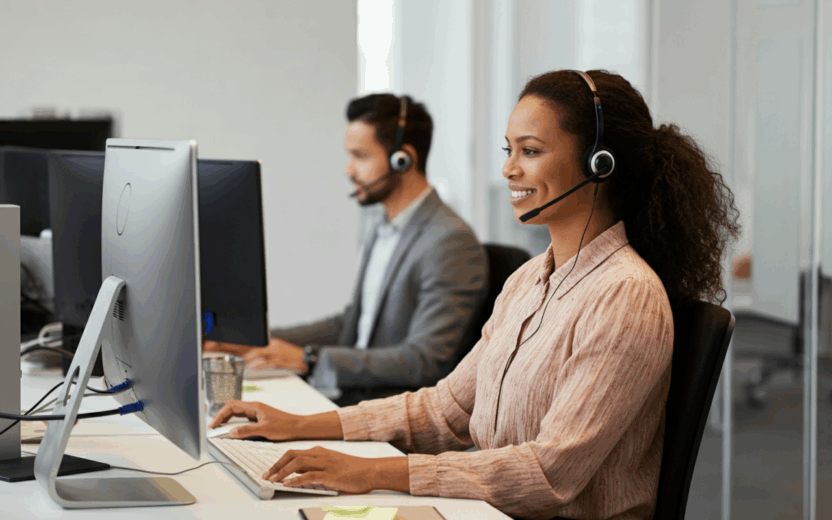 Eine Frau und ein Mann mit Headsets sitzen am PC und telefonieren mit Kund:innen