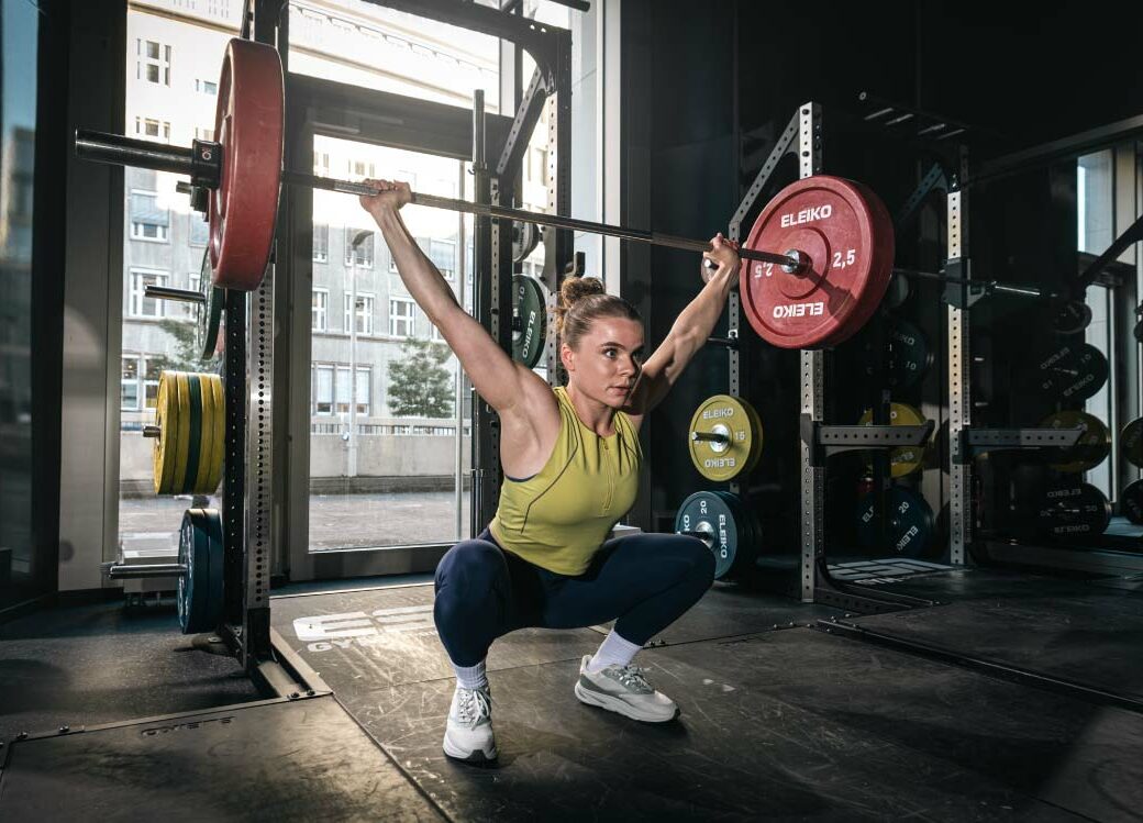 Junge Frau beim Gewichtheben im Sportstudio, toptit dank der Produkte von The Quality Group (TQG). TQG steigert die eigene Performance mit SAP Cloud ERP
