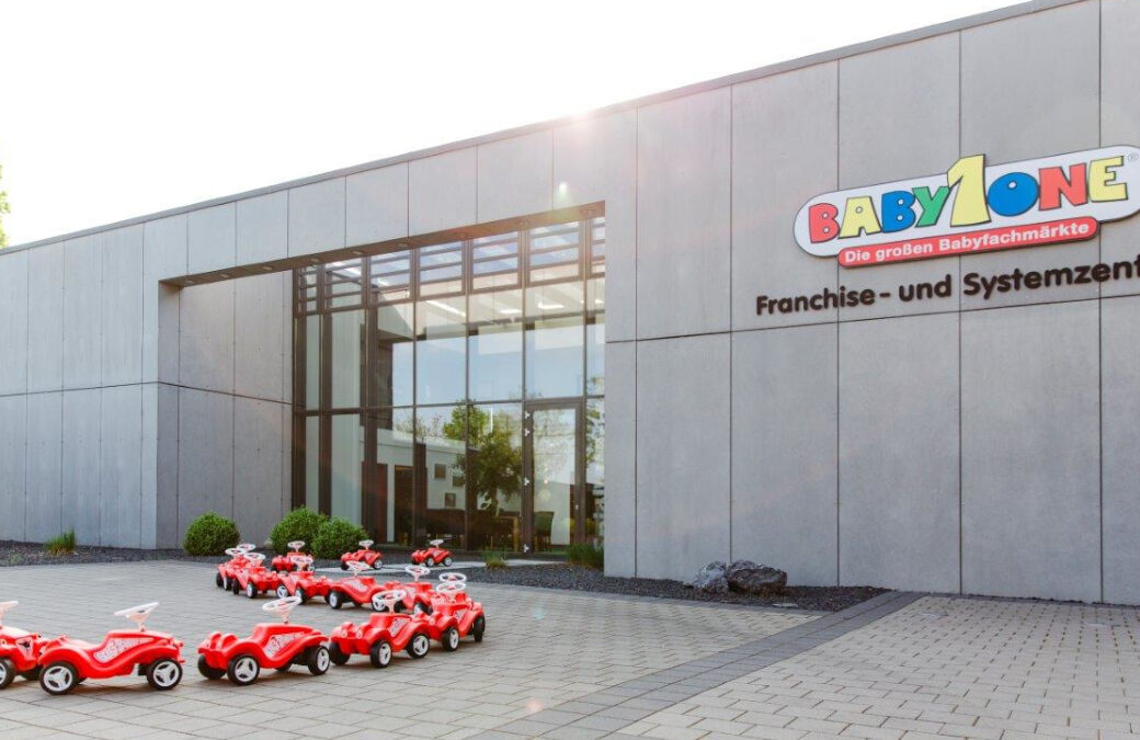 Moderne Franchise-und Systemzentrale im Gewerbepark Münster-Loddenheide. Von dem Eingang stehen kleine rote Bobby Cars