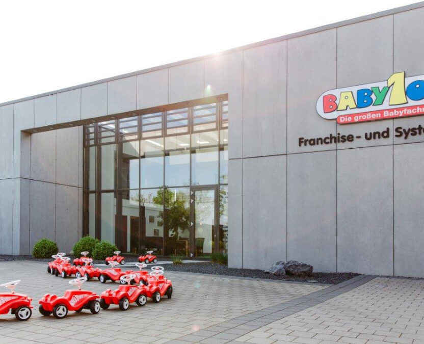 Moderne Franchise-und Systemzentrale im Gewerbepark Münster-Loddenheide. Von dem Eingang stehen kleine rote Bobby Cars