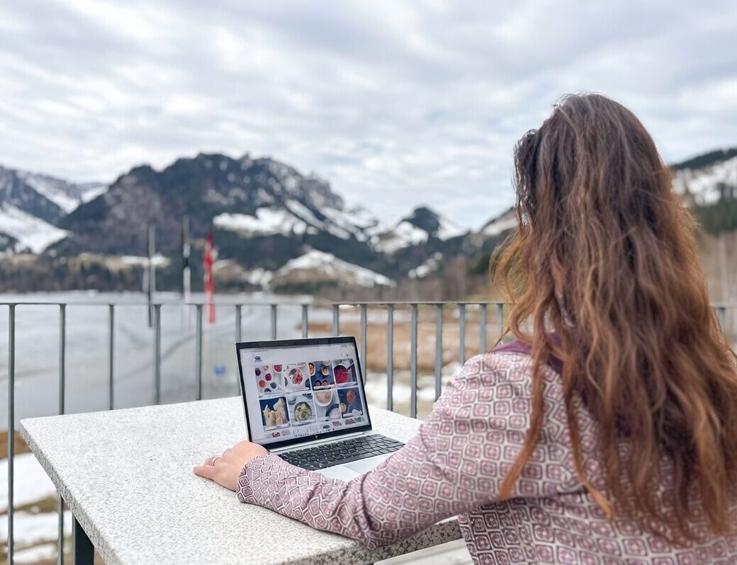 Eine Frau nutzt ihren Laptop, während sie entspannt auf einem Balkon sitzt.