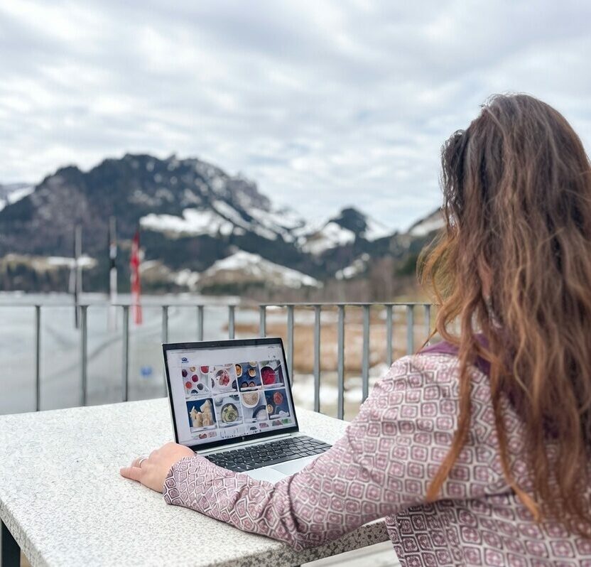 Eine Frau nutzt ihren Laptop, während sie entspannt auf einem Balkon sitzt.