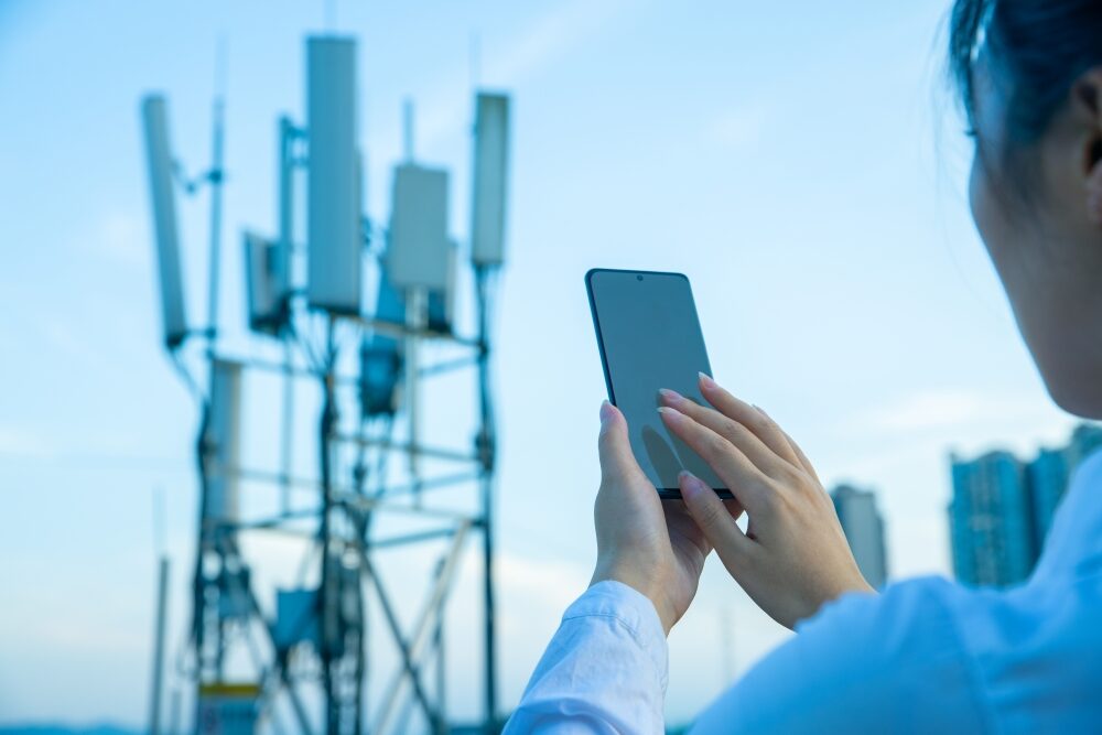 Menschliche Hand mit Mobiltelefon in der Nähe von 4G, 5G Kommunikationsturm