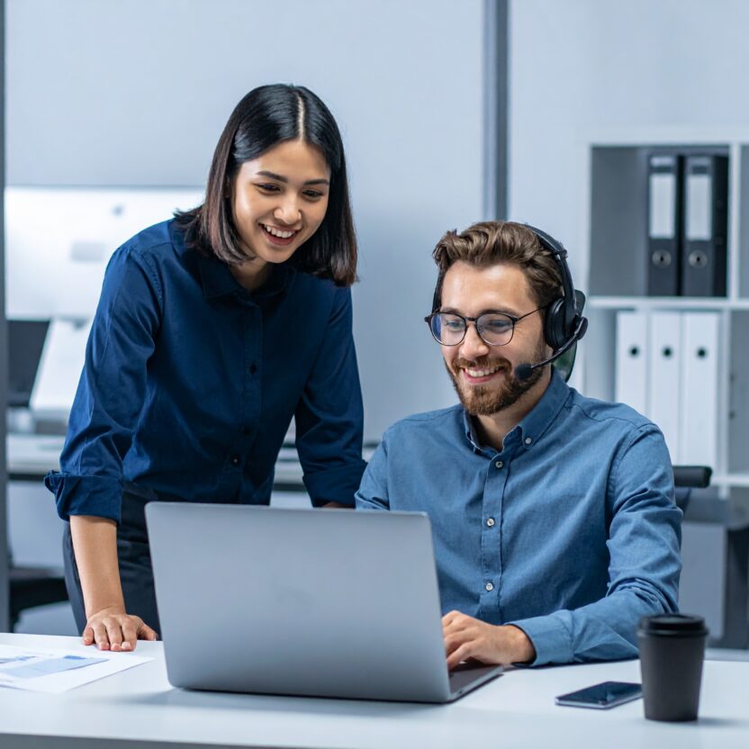 coding specialist working in an office on his laptop. with a headset on smiling.
