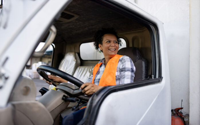 A woman driving a delivery truck. She smiles friendly from the driver's seat