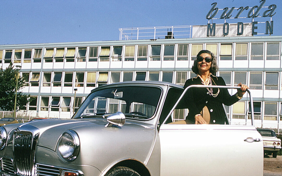 Woman in nostalgic style next to a car from the 1950s, with the Burda Moden building in the background.
