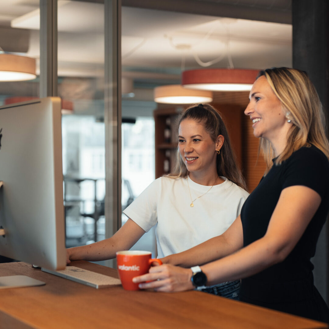 Two women stand at a standing desk and look together at a large screen in a modern office