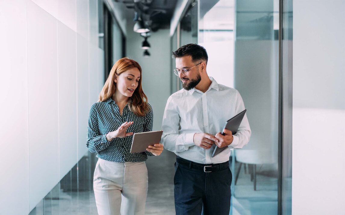 Dos compañeros de trabajo conversan en una oficina moderna. Un hombre y una mujer de negocios en una reunión utilizando una tableta digital y discutiendo sobre estrategia empresarial. Empresarios confiados trabajando juntos en la oficina. Empresarios creativos discutiendo un nuevo proyecto y compartiendo ideas en el lugar de trabajo.