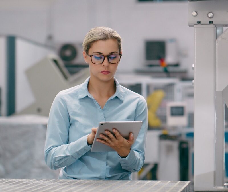 Frau steht in einer High-Tech-Produktionslinie und arbeitet mit ihrem Tablet