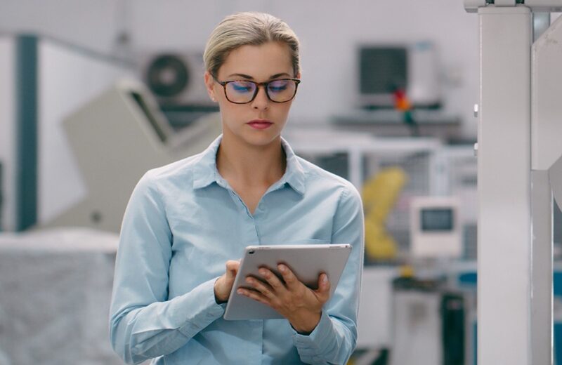 Frau steht in einer High-Tech-Produktionslinie und arbeitet mit ihrem Tablet