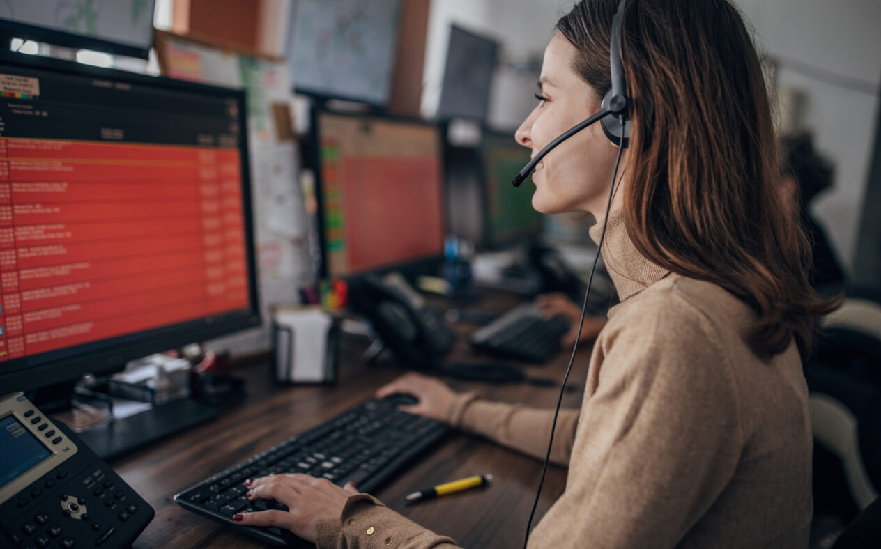 Service-Mitarbeitende mit Headset vor einem PC-Monitor bearbeitet eine Kundenanfrage im Service mit KI