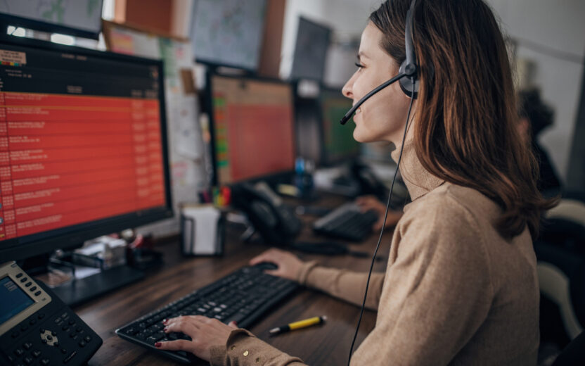 A customer service agent wearing a headset and sitting in front of a computer monitor uses AI in customer service to process a request.