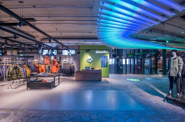 Interior view of Sporthaus Schuster, featuring modern store design, outdoor clothing, an information desk, and stylish lighting.