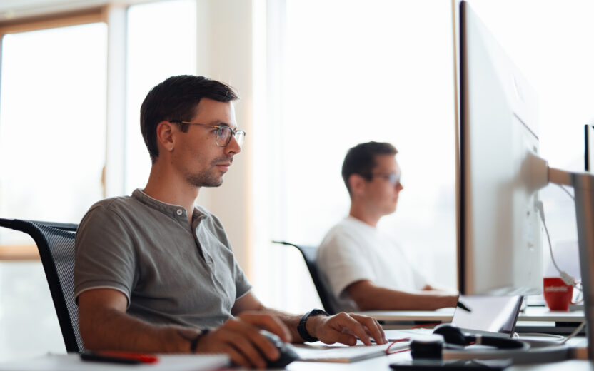 Two employees are working intently at their desks on their computers.