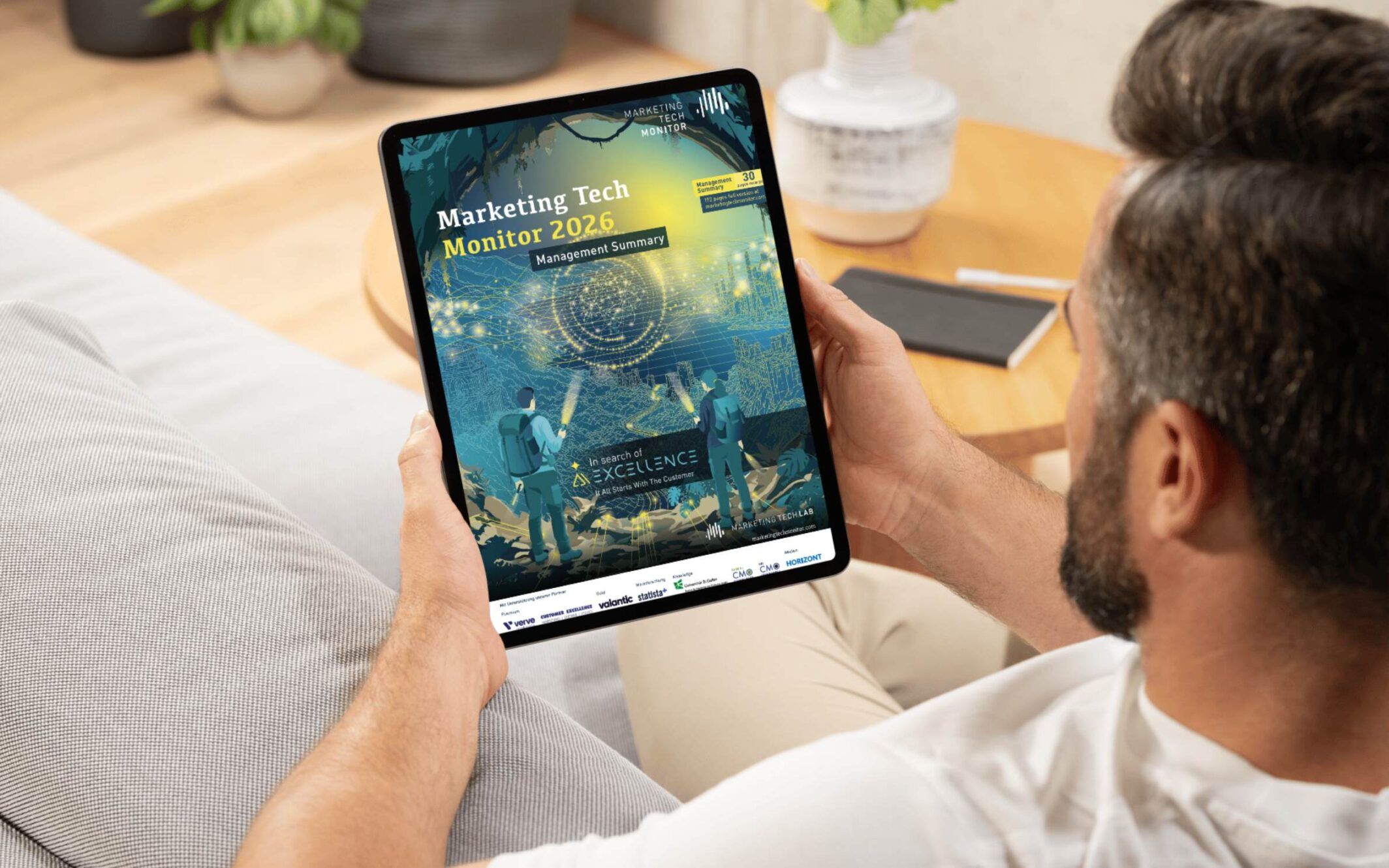 Mann auf einem Sofa liest die Management Summary zum Marketing Tech Monitor 2026 auf einem Tablet, um zu erfahren, wie wie Marketing KI-ready wird. 