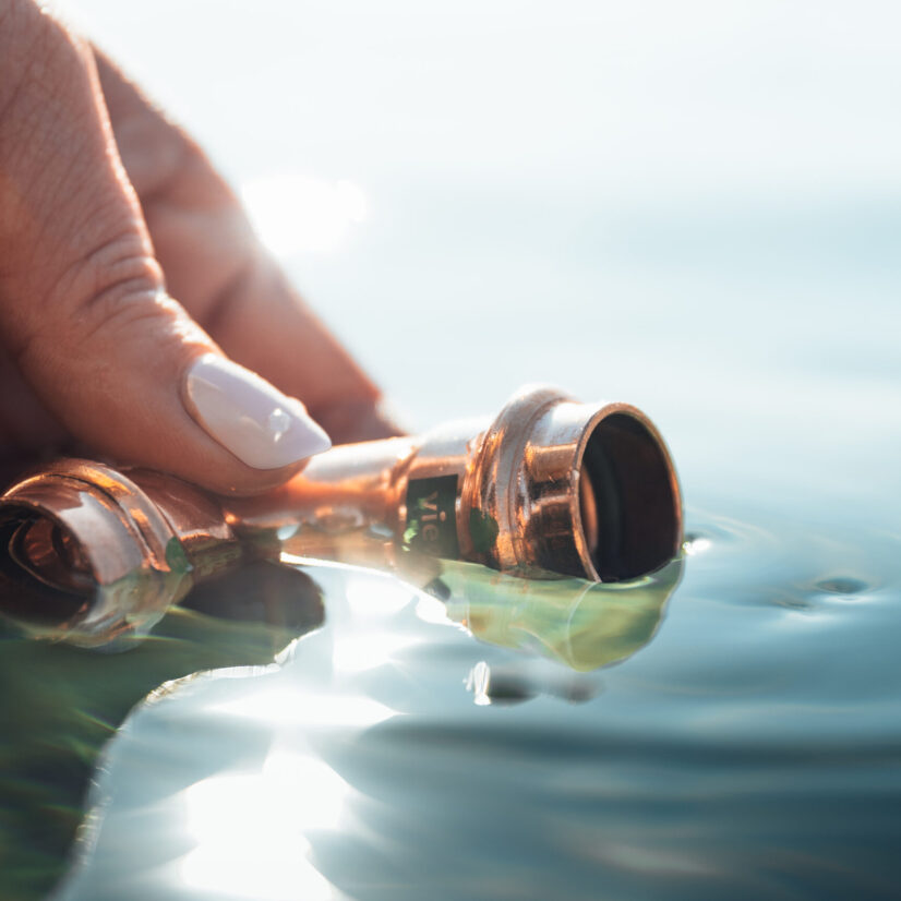 Eine Hand hält ein Viega-Bauteil ins Wasser.