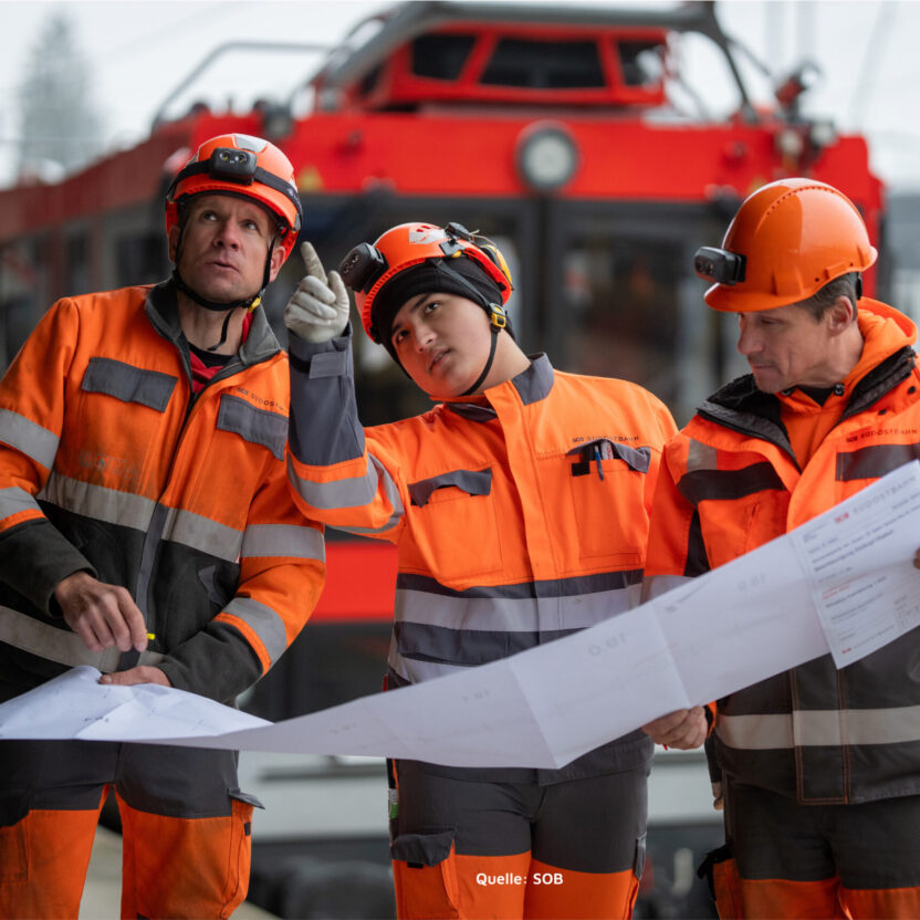 Three men working constructions in rail, looking at map.