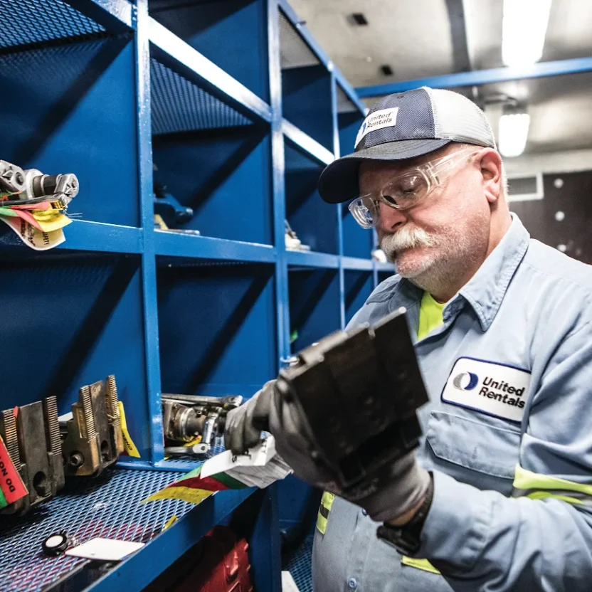 Technician inspecting a tool part in a tool crib with tagged equipment on blue shelving
