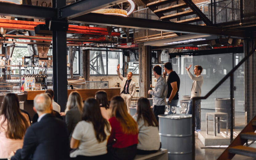 Personen sitzen in einem industriellen Office und hören einen Vortragenden zu.