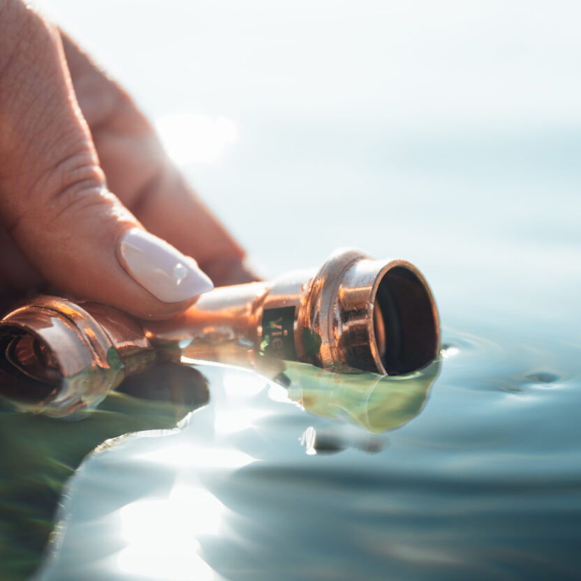 Eine Hand hält ein Viega-Bauteil ins Wasser.