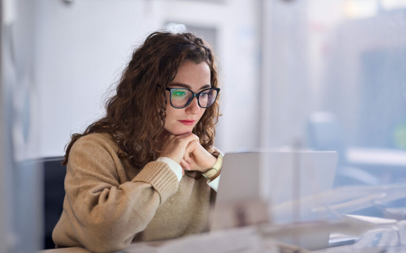 Young woman wearing glasses watching online webinar at work.