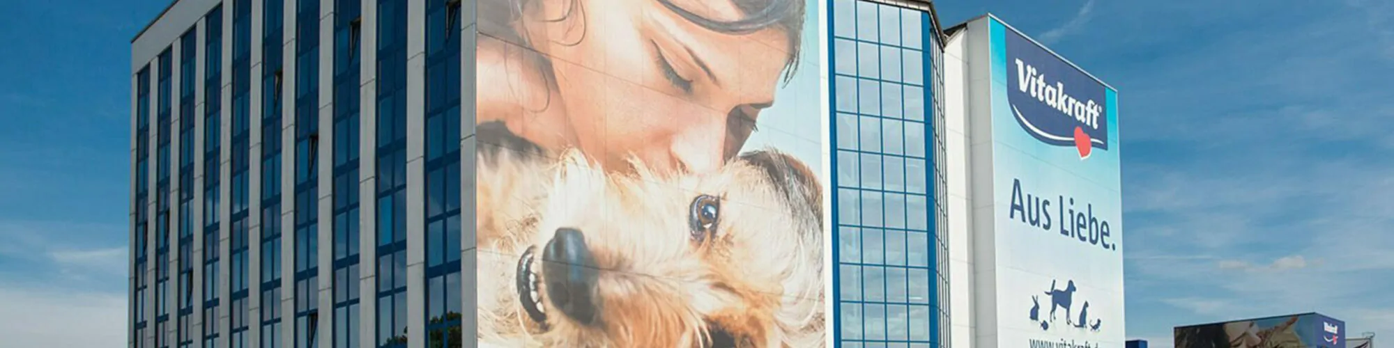 Bild des Firmengebäudes von Vitakraft mit Poster einer Frau die ihren Hund küsst