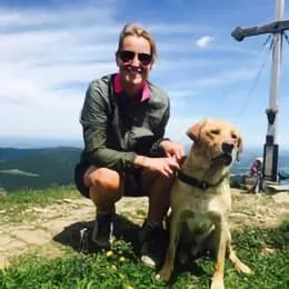 About us - Team - Uta Heiss, Management Assistance bei valantic, mit einem Hund auf einem Berg und Gipfelkreuz im Hintergrund